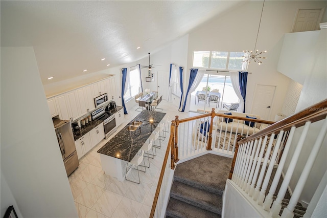 kitchen featuring white cabinetry, stainless steel appliances, high vaulted ceiling, a breakfast bar, and ceiling fan with notable chandelier