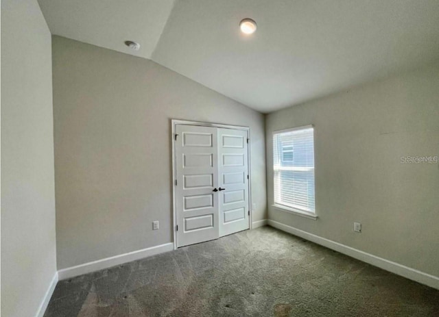 unfurnished bedroom with a closet, dark carpet, and lofted ceiling