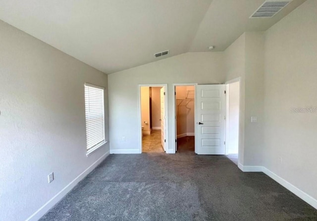 unfurnished bedroom featuring a spacious closet, a closet, dark carpet, and vaulted ceiling