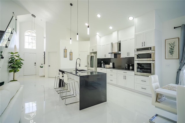 kitchen featuring tasteful backsplash, wall chimney exhaust hood, a kitchen island with sink, decorative light fixtures, and white cabinetry