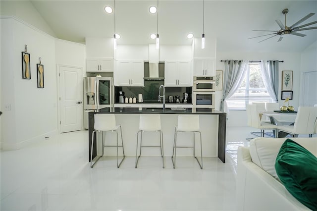 kitchen with white cabinets, wall chimney range hood, hanging light fixtures, vaulted ceiling, and appliances with stainless steel finishes