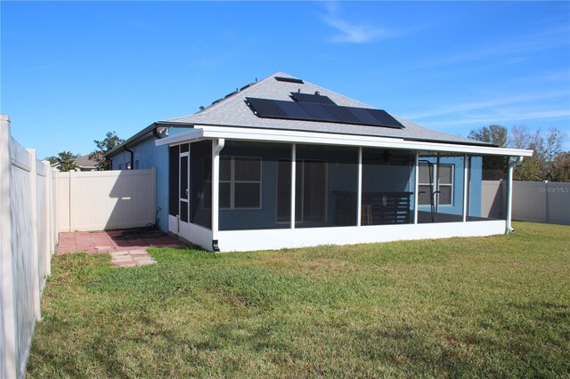 rear view of house featuring a sunroom, a yard, and solar panels