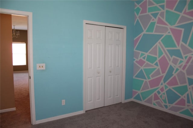 unfurnished bedroom featuring an inviting chandelier, dark carpet, and a closet