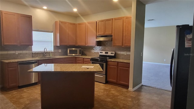 kitchen with sink, appliances with stainless steel finishes, a center island, light stone counters, and decorative backsplash