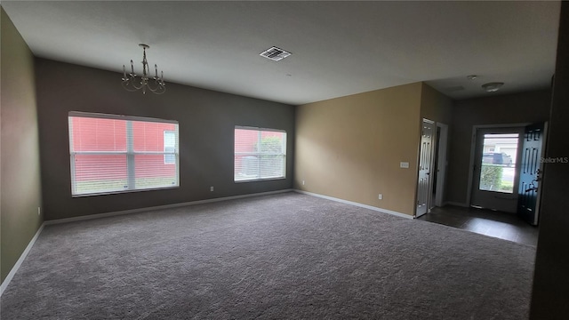 spare room with dark colored carpet and an inviting chandelier