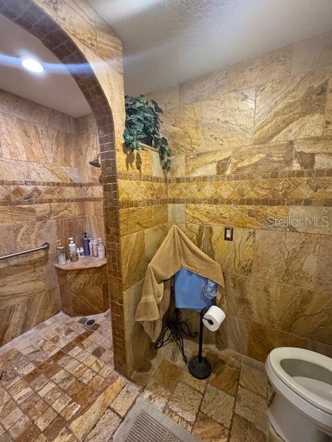 bathroom featuring a shower, tile walls, and toilet