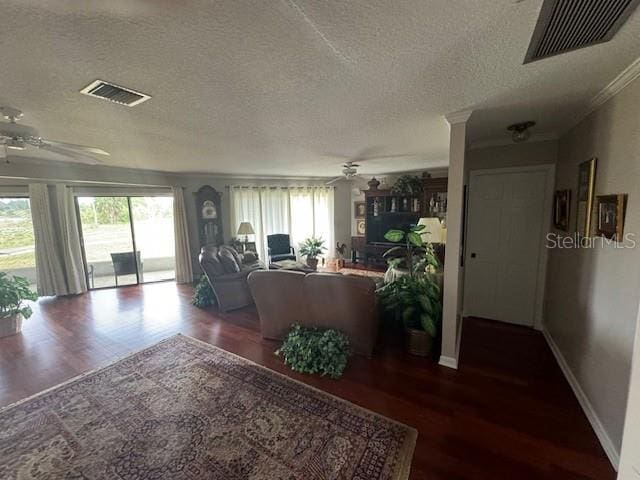 living room featuring ceiling fan, ornamental molding, a textured ceiling, and dark wood-type flooring