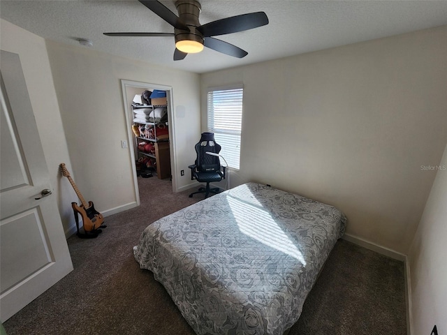 bedroom featuring a textured ceiling, ceiling fan, dark colored carpet, a spacious closet, and a closet