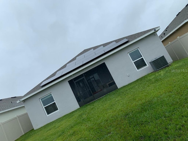 back of house with a lawn, central AC, a sunroom, and solar panels