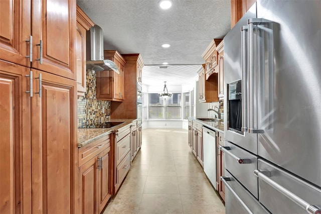 kitchen featuring pendant lighting, wall chimney range hood, high quality fridge, dishwashing machine, and light stone counters