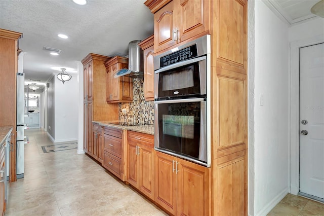 kitchen featuring backsplash, wall chimney exhaust hood, light stone countertops, a textured ceiling, and stainless steel appliances