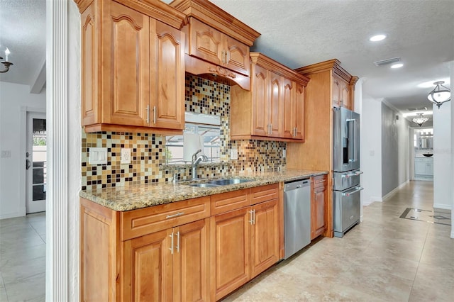 kitchen featuring sink, light stone counters, backsplash, a textured ceiling, and appliances with stainless steel finishes