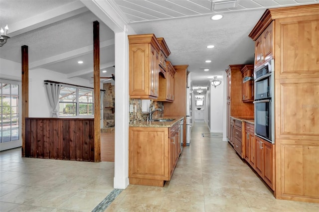 kitchen featuring light stone countertops, appliances with stainless steel finishes, a textured ceiling, sink, and beam ceiling