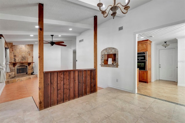 interior space featuring ceiling fan with notable chandelier, a textured ceiling, lofted ceiling with beams, a stone fireplace, and light tile patterned flooring