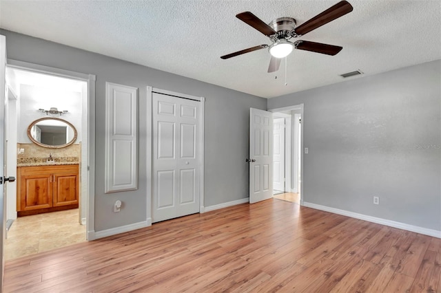 unfurnished bedroom featuring ceiling fan, sink, light hardwood / wood-style flooring, ensuite bathroom, and a textured ceiling