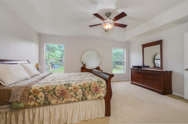 bedroom featuring a raised ceiling, multiple windows, ceiling fan, and light colored carpet