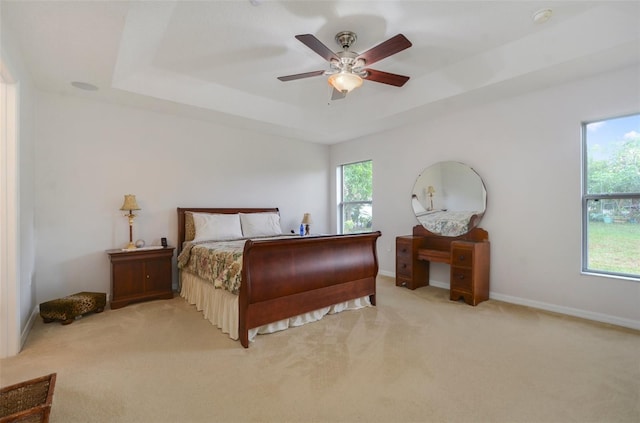 bedroom featuring ceiling fan, light carpet, and a tray ceiling