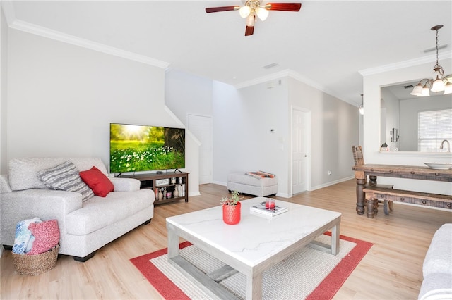 living room featuring ceiling fan with notable chandelier, light wood-type flooring, crown molding, and sink