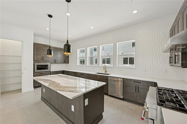 kitchen featuring decorative light fixtures, a center island, sink, stainless steel appliances, and light stone counters