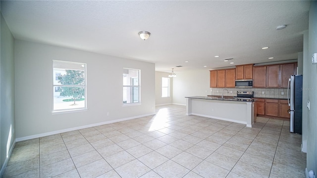 kitchen featuring decorative backsplash, a wealth of natural light, stainless steel appliances, and a kitchen island with sink