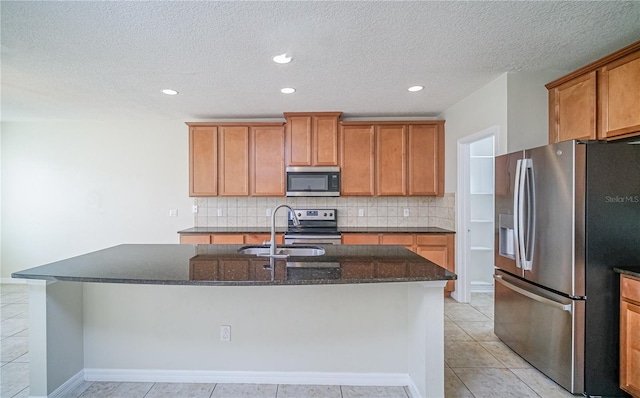 kitchen featuring backsplash, dark stone counters, stainless steel appliances, light tile patterned floors, and an island with sink