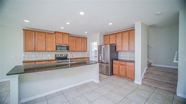 kitchen featuring stainless steel appliances, a kitchen island with sink, sink, light tile patterned floors, and dark stone countertops