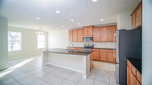 kitchen with a kitchen island with sink, sink, decorative backsplash, light tile patterned floors, and appliances with stainless steel finishes