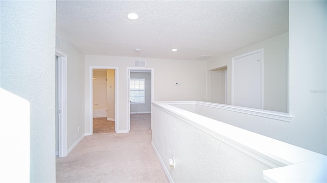 corridor with light colored carpet and a textured ceiling