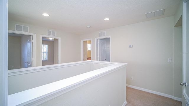 hall featuring light colored carpet and a textured ceiling