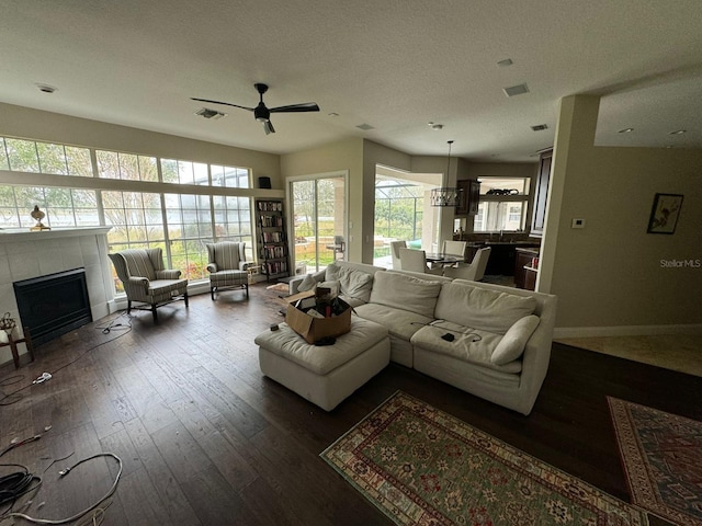 living room with dark hardwood / wood-style floors, ceiling fan, a textured ceiling, and a tile fireplace