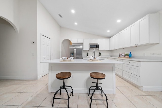 kitchen with a breakfast bar, stainless steel appliances, a center island with sink, white cabinets, and lofted ceiling