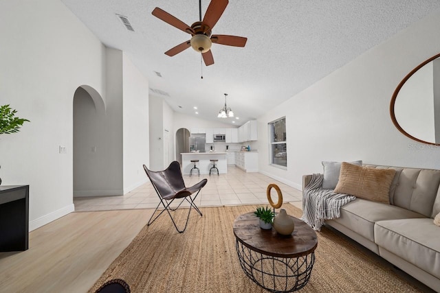 living room featuring ceiling fan with notable chandelier, light tile patterned floors, a textured ceiling, and vaulted ceiling