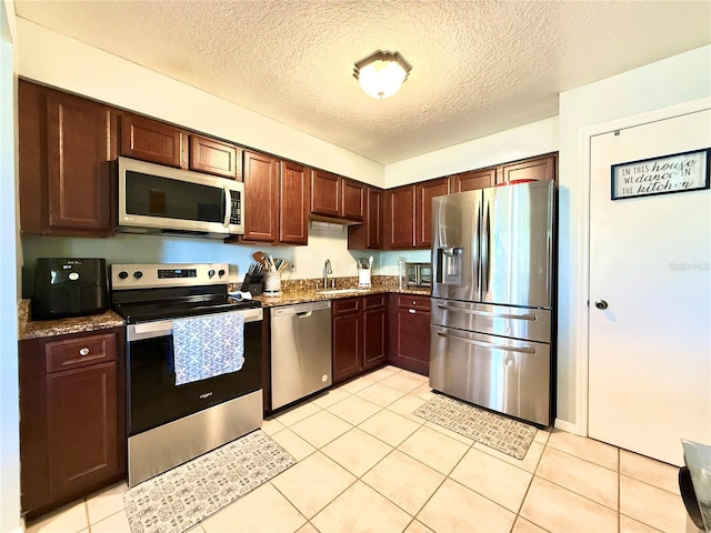 kitchen with appliances with stainless steel finishes, a textured ceiling, sink, stone countertops, and light tile patterned flooring