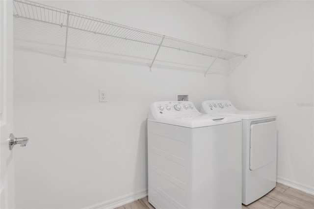 clothes washing area with washing machine and dryer and light wood-type flooring