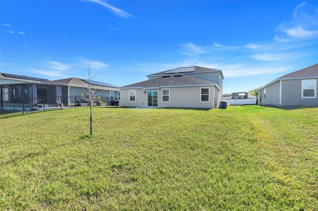 rear view of property featuring central AC, a lawn, a sunroom, and solar panels