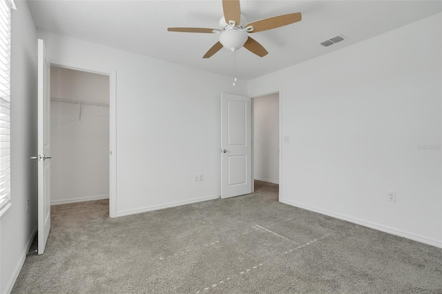 unfurnished bedroom with a walk in closet, light carpet, ceiling fan, and a closet