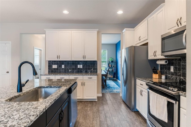 kitchen featuring backsplash, light stone counters, stainless steel appliances, sink, and white cabinetry