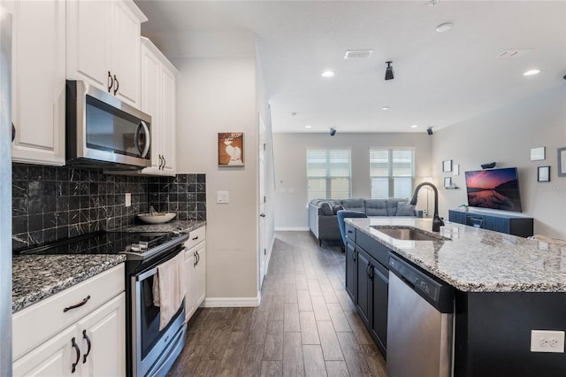 kitchen featuring white cabinets, a center island with sink, sink, decorative backsplash, and appliances with stainless steel finishes