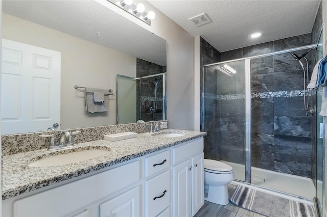 bathroom with vanity, a shower with shower door, a textured ceiling, and toilet