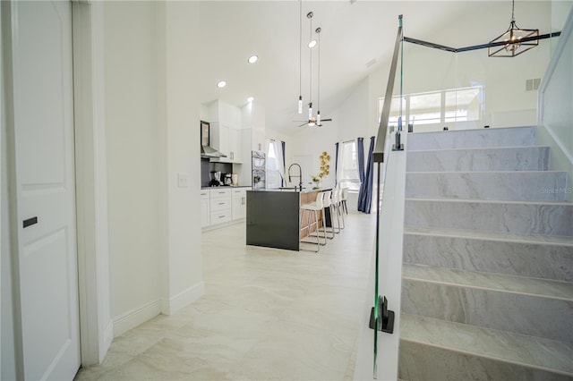 stairs with ceiling fan with notable chandelier, lofted ceiling, and sink