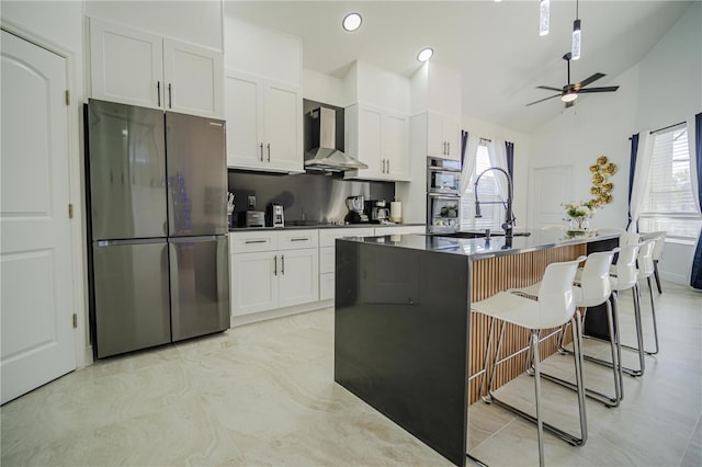 kitchen with white cabinetry, wall chimney exhaust hood, an island with sink, and appliances with stainless steel finishes