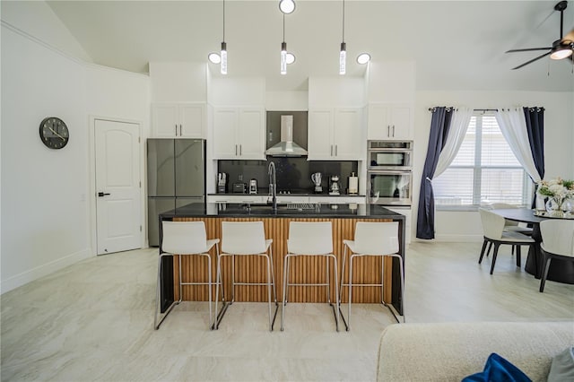 kitchen featuring white cabinets, wall chimney exhaust hood, a kitchen island with sink, and vaulted ceiling