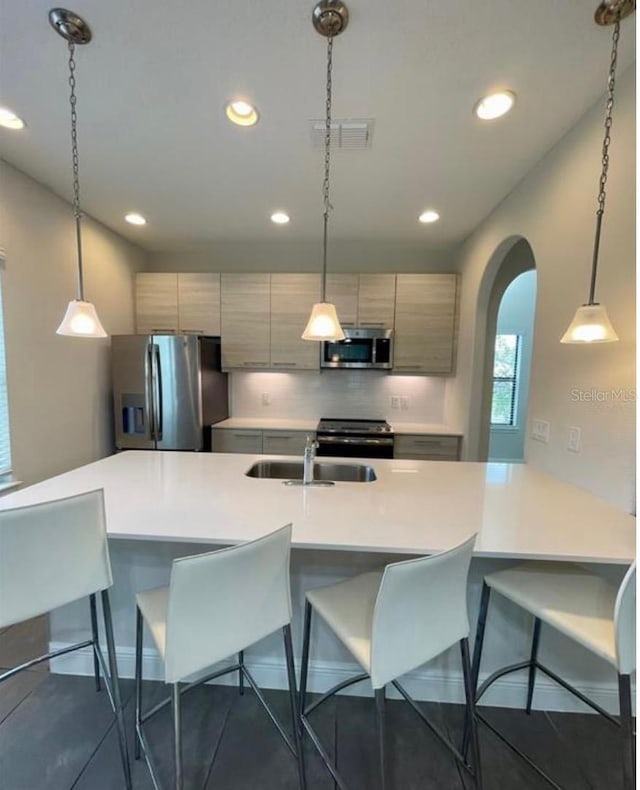 kitchen featuring a breakfast bar, sink, appliances with stainless steel finishes, pendant lighting, and backsplash