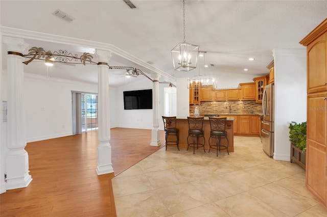 kitchen featuring ceiling fan, a kitchen breakfast bar, decorative columns, crown molding, and a kitchen island