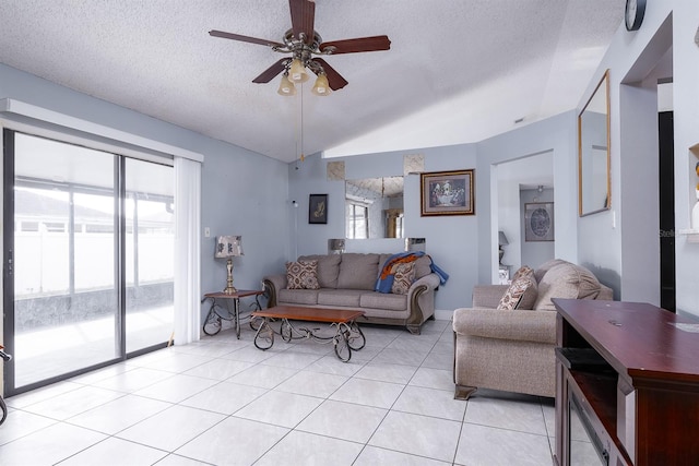 living room with ceiling fan, a textured ceiling, light tile patterned floors, and vaulted ceiling