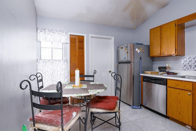 kitchen with vaulted ceiling, sink, light tile patterned flooring, appliances with stainless steel finishes, and a textured ceiling