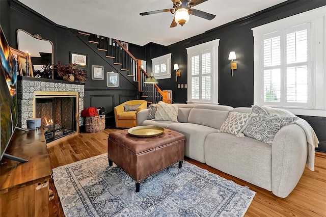 living area featuring stairs, a decorative wall, wood finished floors, and a lit fireplace