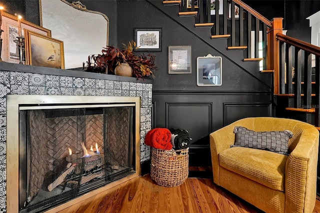 sitting room with stairs, a decorative wall, wood finished floors, and a tile fireplace