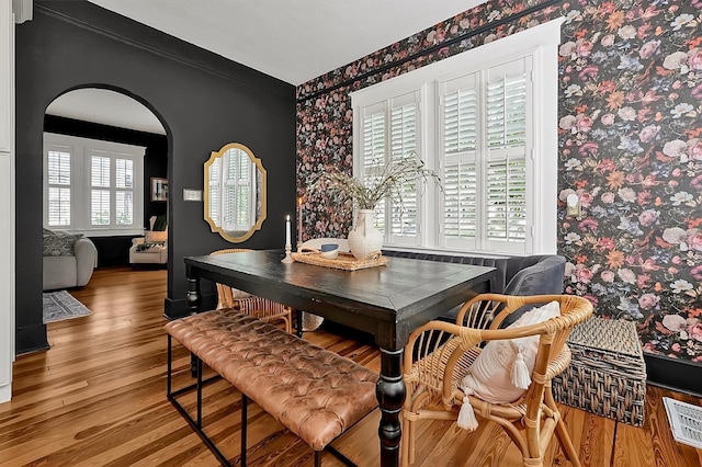 dining area featuring visible vents, arched walkways, wood finished floors, and wallpapered walls