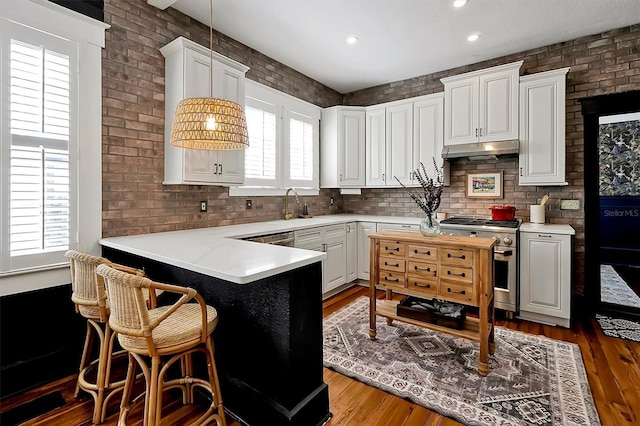 kitchen with under cabinet range hood, high end stainless steel range oven, wood finished floors, and brick wall